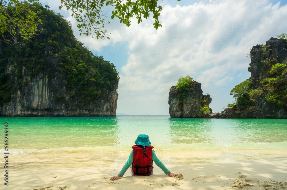 Fototapeta premium back asian child or kid girl sitting alone on beach or blue sea and wear life jacket and hat on white sand by mountain view for vacation travel on summer holiday relax at hong island krabi in thailand