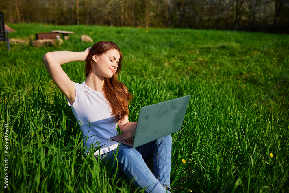 on a clear sunny day, a happy woman works sitting at a laptop in the field