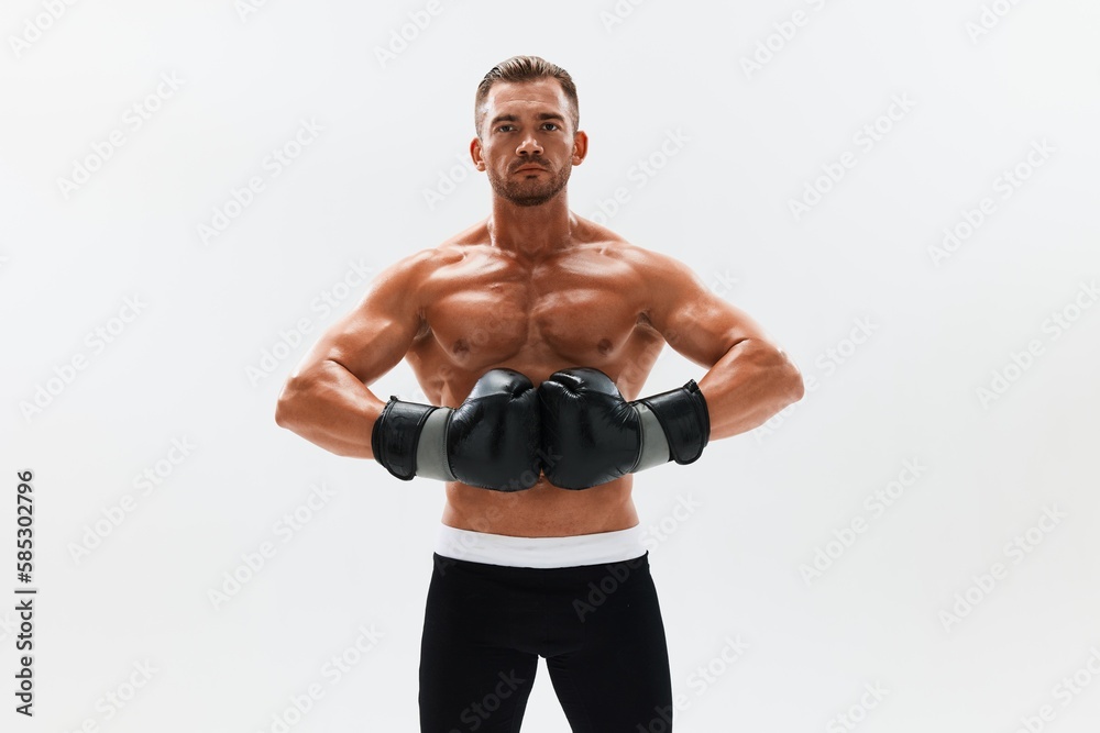 Man athletic bodybuilder poses in boxing gloves with nude torso abs in full-length background, boxing and martial arts. Advertising, sports, active lifestyle, competition, challenge concept. 