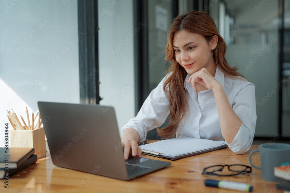 Image of a young beautiful brooding Asian woman working with a laptop while sitting at a laptop in the office, thinking of a professional plan, project management, and considering new business ideas. Image of a young beautiful brooding Asian woman working with a laptop while sitting at a laptop in the office, thinking of a professional plan, project management, and considering new business ideas.