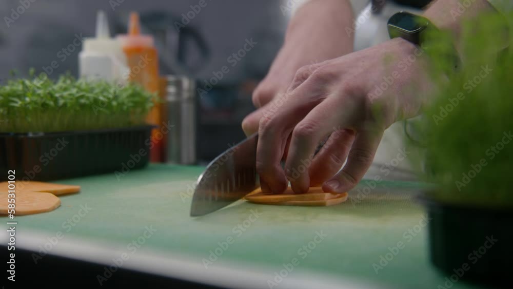 The cook cuts sweet potato on cutting board. Hands of professional chef close-up. Greenery and other ingredients on kitchen desk. Process of cooking gourmet dish. Public catering. Vegetarian dish. The cook cuts sweet potato on cutting board. Hands of professional chef close-up. Greenery and other ingredients on kitchen desk. Process of cooking gourmet dish. Public catering. Vegetarian dish.