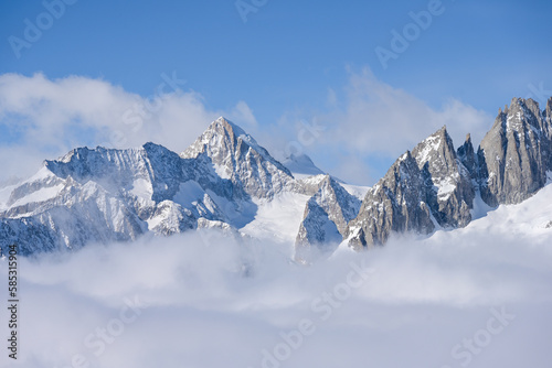 Snow covered mountains in winter, above clouds, Nesthorn with Breithorn and Fusshoerner in the Swiss Alps - with blue sky