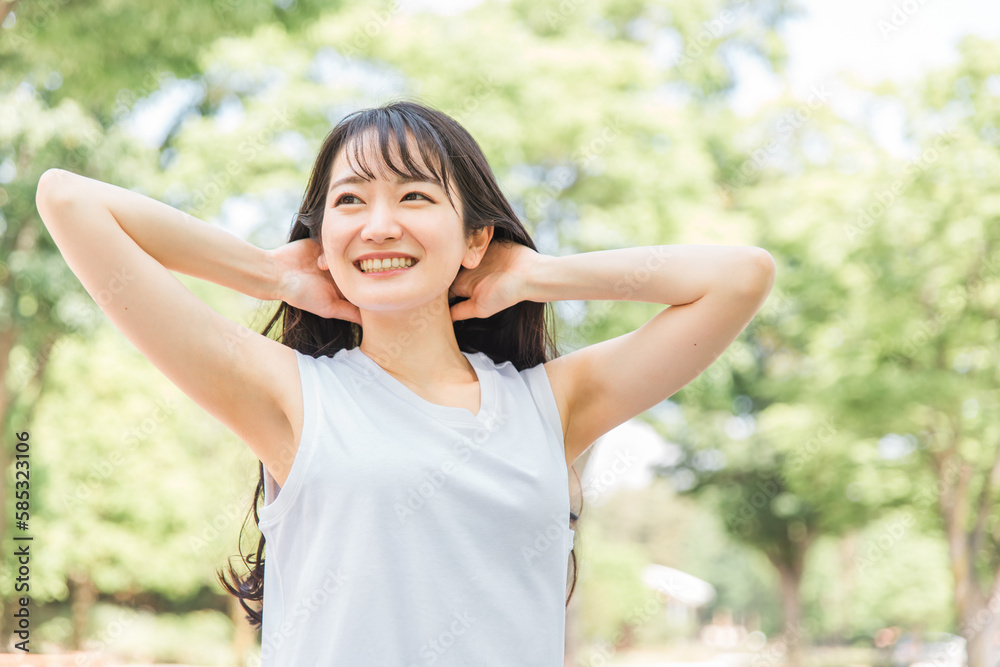 新緑の中で髪を触る笑顔の日本人女性（ヘアケア・シャンプー・美髪）
