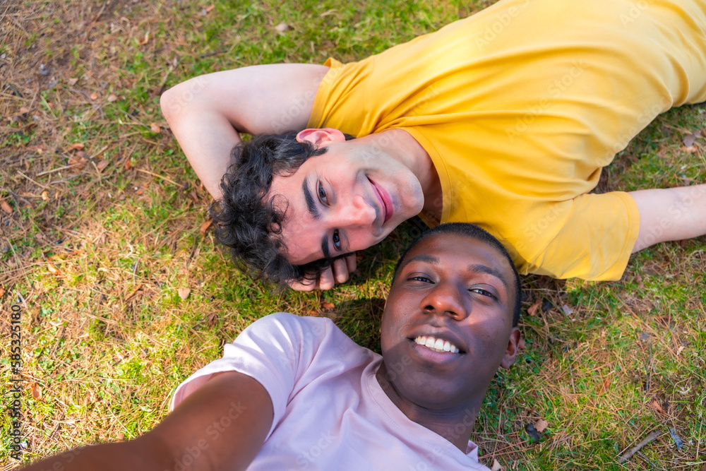 Couple of multi-ethnic men in a park, lgbt concept, lying on the grass taking a selfie Couple of multi-ethnic men in a park, lgbt concept, lying on the grass taking a selfie