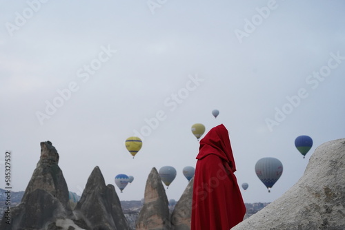 A man in the desert against the background of flying balloons in a red cape with a hood. Cappadocia