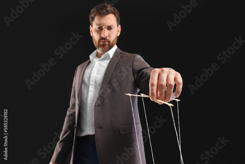 Wallpaper Mural Man in suit pulling strings of puppet on black background, low angle view