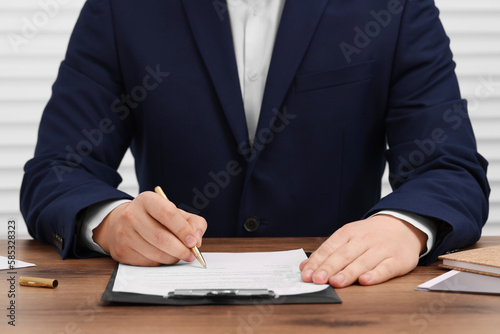 Man signing document at wooden table, closeup