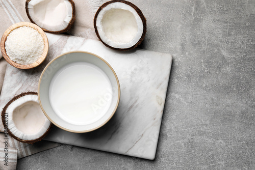 Bowl of delicious coconut milk  flakes and coconuts on light grey table  flat lay. Space for text