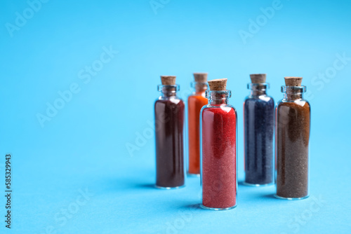Glass bottles with different food coloring on light blue background. Space for text