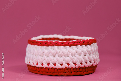 Crochet Home Basket on pink background. Red and white round box for small things made of thread crocheted, handmade art. Front view.