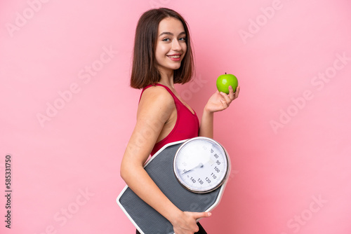 Young Ukrainian woman isolated on pink background with weighing machine and with an apple