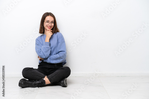 Young Ukrainian woman sitting on the floor isolated on white background with glasses and smiling