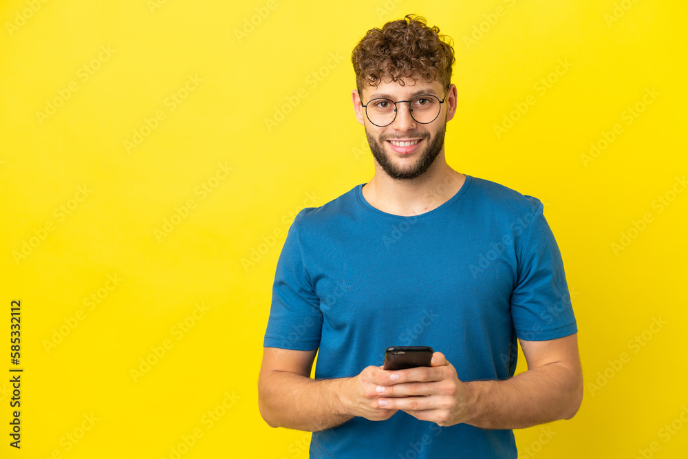 Young handsome caucasian man isolated on yellow background sending a message with the mobile Young handsome caucasian man isolated on yellow background sending a message with the mobile