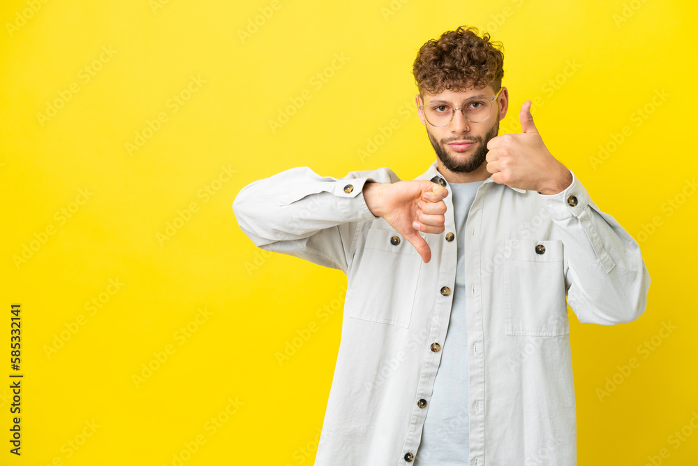 Young handsome caucasian man isolated on yellow background making good-bad sign. Undecided between yes or not Young handsome caucasian man isolated on yellow background making good-bad sign. Undecided between yes or not