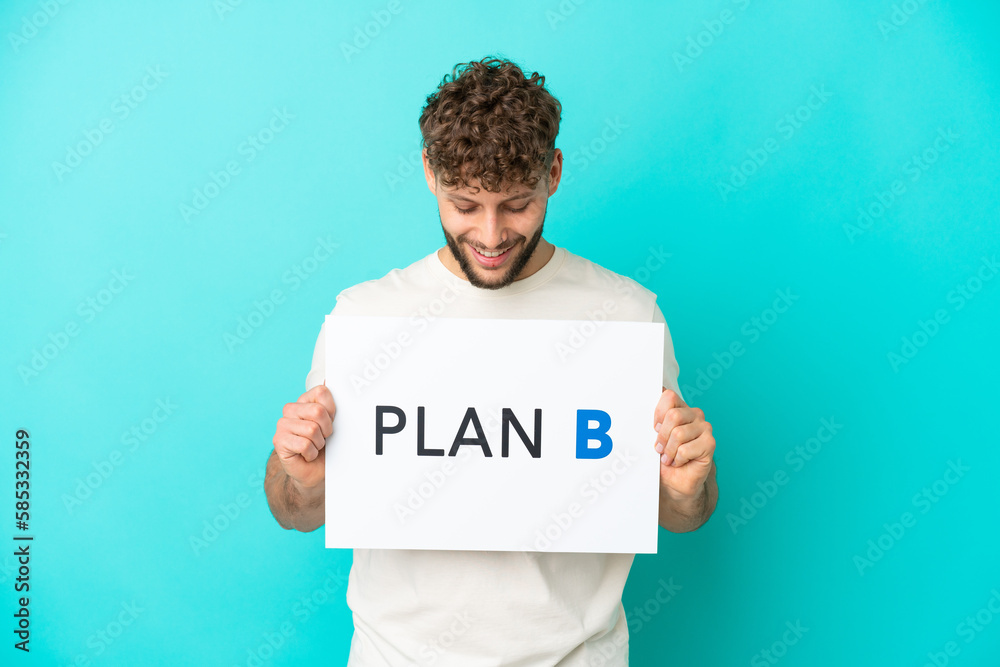 Young handsome caucasian man isolated on blue background holding a placard with the message PLAN B