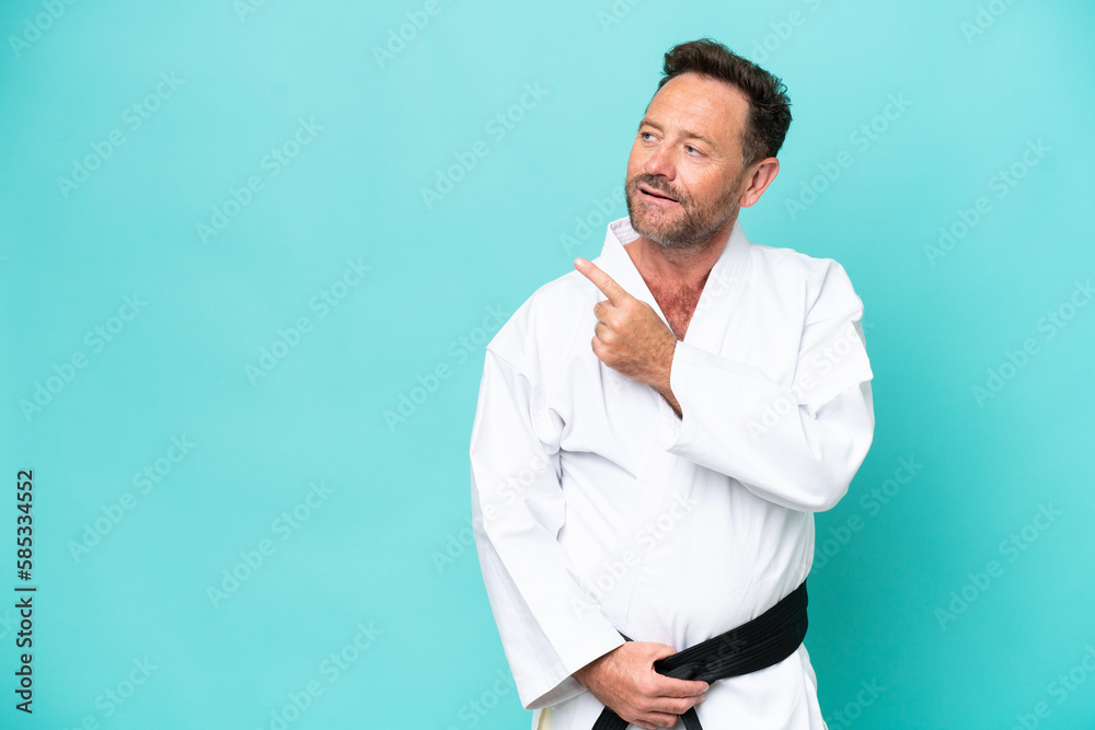 Middle age caucasian man isolated on blue background doing karate and pointing to the lateral Middle age caucasian man isolated on blue background doing karate and pointing to the lateral