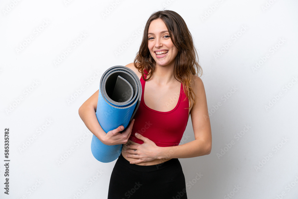 Young sport caucasian woman going to yoga classes while holding a mat isolated on white background smiling a lot