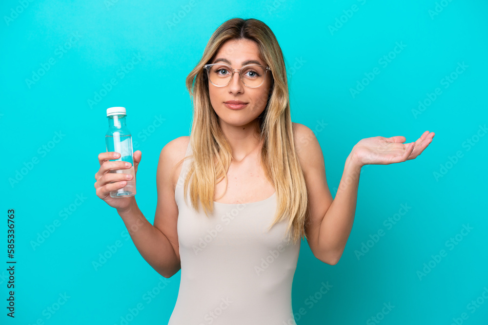 Young Uruguayan woman with a bottle of water isolated on blue background having doubts while raising hands Young Uruguayan woman with a bottle of water isolated on blue background having doubts while raising hands