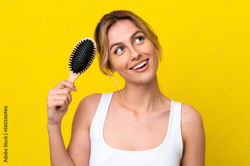 Young Uruguayan woman with hair comb isolated on yellow background looking up while smiling Young Uruguayan woman with hair comb isolated on yellow background looking up while smiling