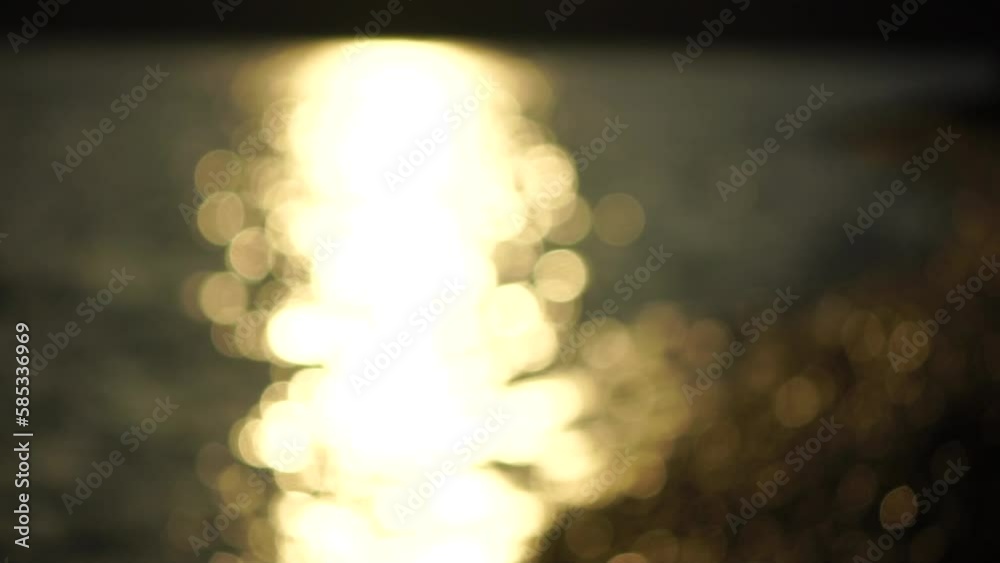 Blurred golden sea at sunset with shifting focus and bokeh effect. Sun reflects and sparkles on waves, illuminating golden sea. Holiday recreation concept. Abstract nautical summer ocean sunset nature