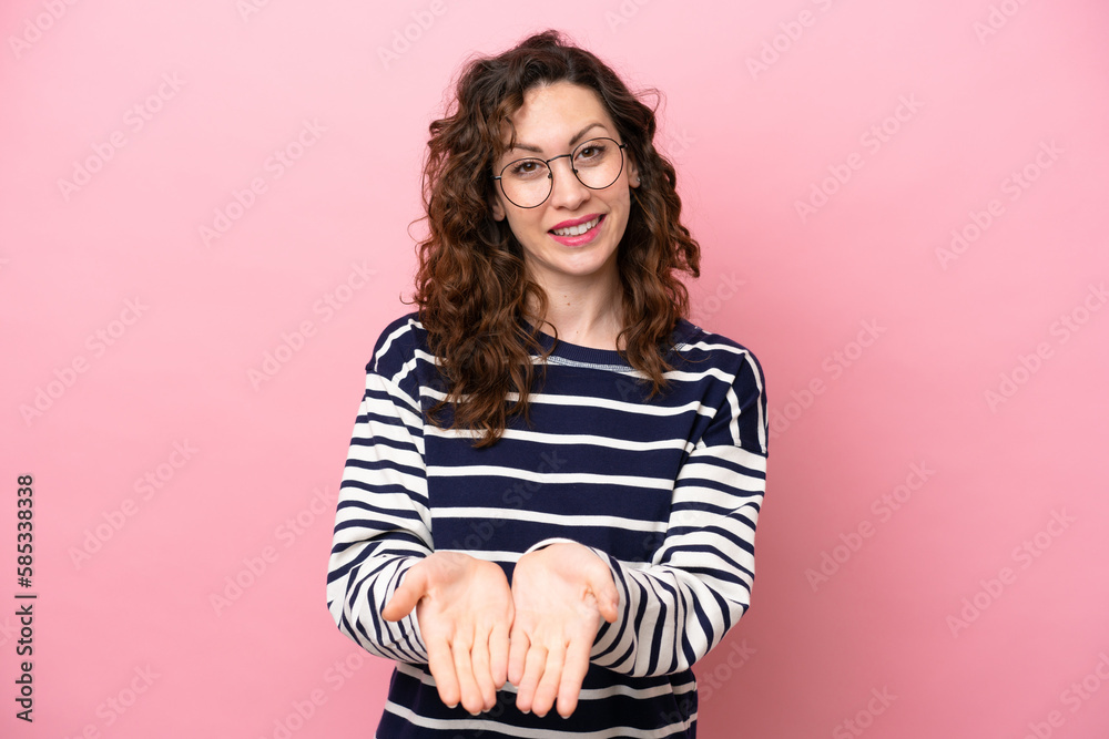 Young caucasian woman isolated on pink background holding copyspace imaginary on the palm to insert an ad Young caucasian woman isolated on pink background holding copyspace imaginary on the palm to insert an ad
