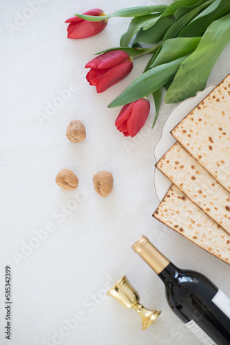 Matzah on white plate with red tulips, bottle of wine and walnut on white background. Traditional Holiday on Passover. Home symbol of lovely Jewish family in pesach. top view
