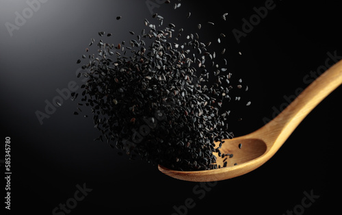 Grains of black sesame is poured with a wooden spoon.