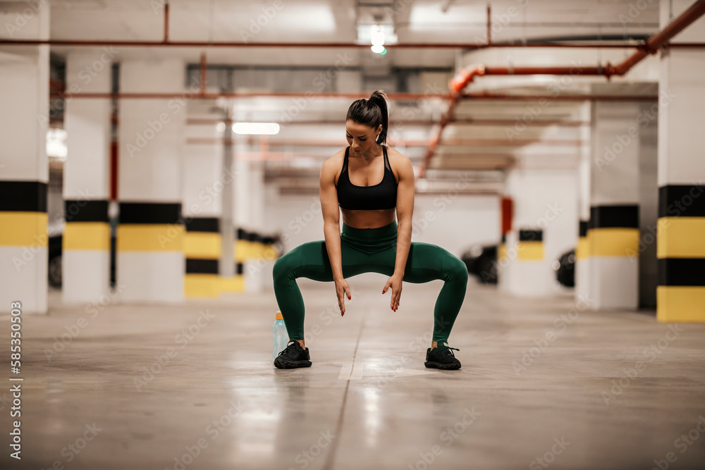 A muscular sportswoman in shape is doing squats in urban interior. A muscular sportswoman in shape is doing squats in urban interior.