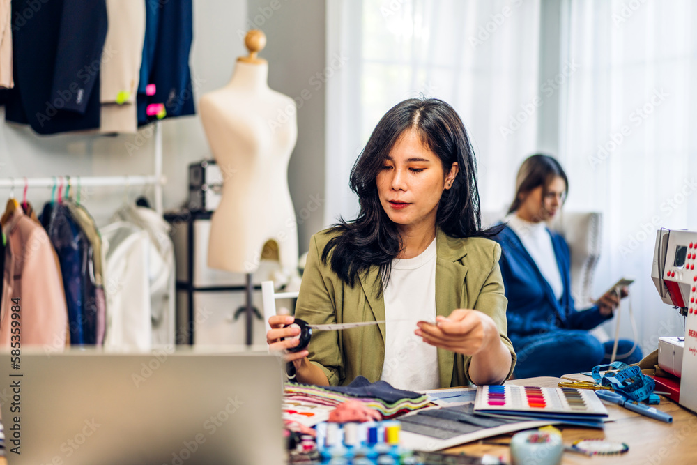 Fototapeta premium Portrait of young beautiful asian woman fashion designer stylish sitting and working with color samples.Attractive young asian girl working with colorful fabrics at fashion studio