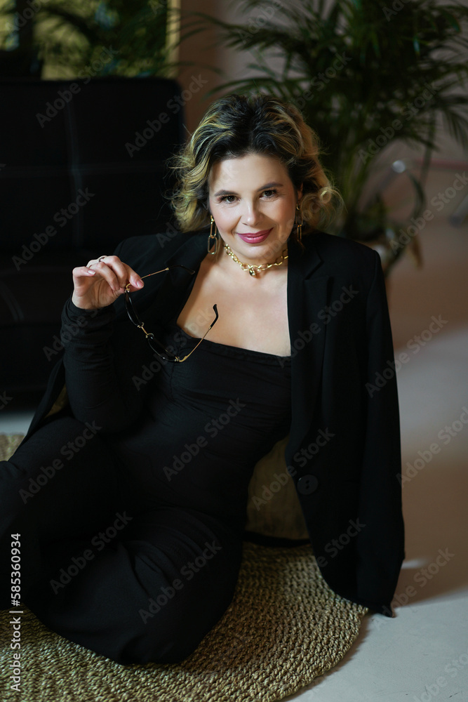 Fototapeta premium A smiling woman in a black suit sits holding glasses.
