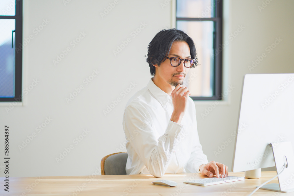 パソコンに向かって考え事をする若い男性 パソコンに向かって考え事をする若い男性