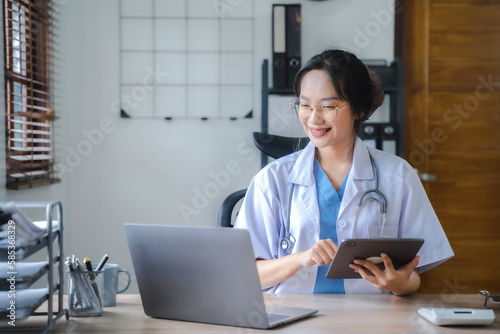 Doctor working on laptop computer and tablet and medical stethoscope on clipboard on desk.