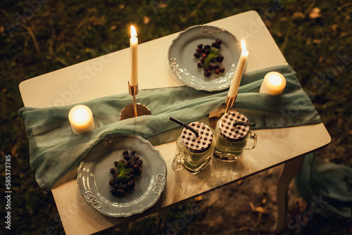 Candles  mulberry plates and cups stand on a festive  decorative table with a cloth at night. Image for your creative design and illustrations.