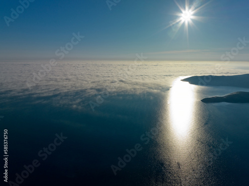 Coast scenic dreamy landscape view silhouette of mountains in fog not far from Budva at Adriatic sea on sunny Summer day with shining Sun rays on blue sky. Drone aerial panorama