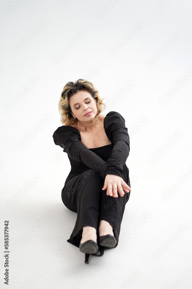 A smiling woman in a black suit is sitting on the floor on a white background. A smiling woman in a black suit is sitting on the floor on a white background.