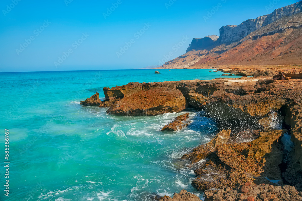 Beach with emerald water and wild red rocky shore.
