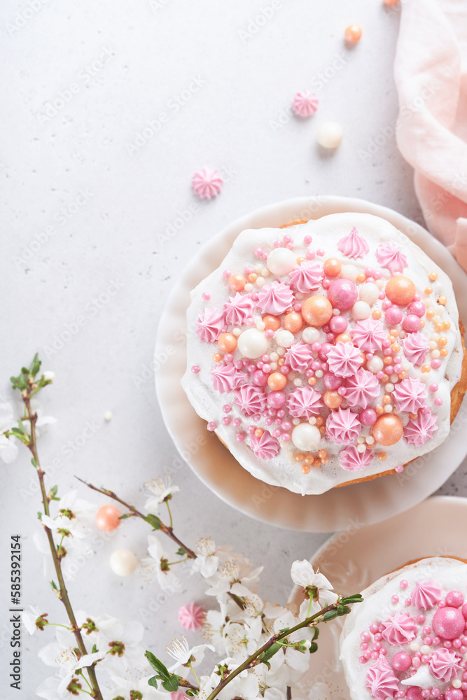 Traditional Easter sweet bread or cakes with white icing and sugar decor, colored eggs and cherry blossom tree branch over white table. Various Spring Easter cakes. Happy Easter day. Selective focus.