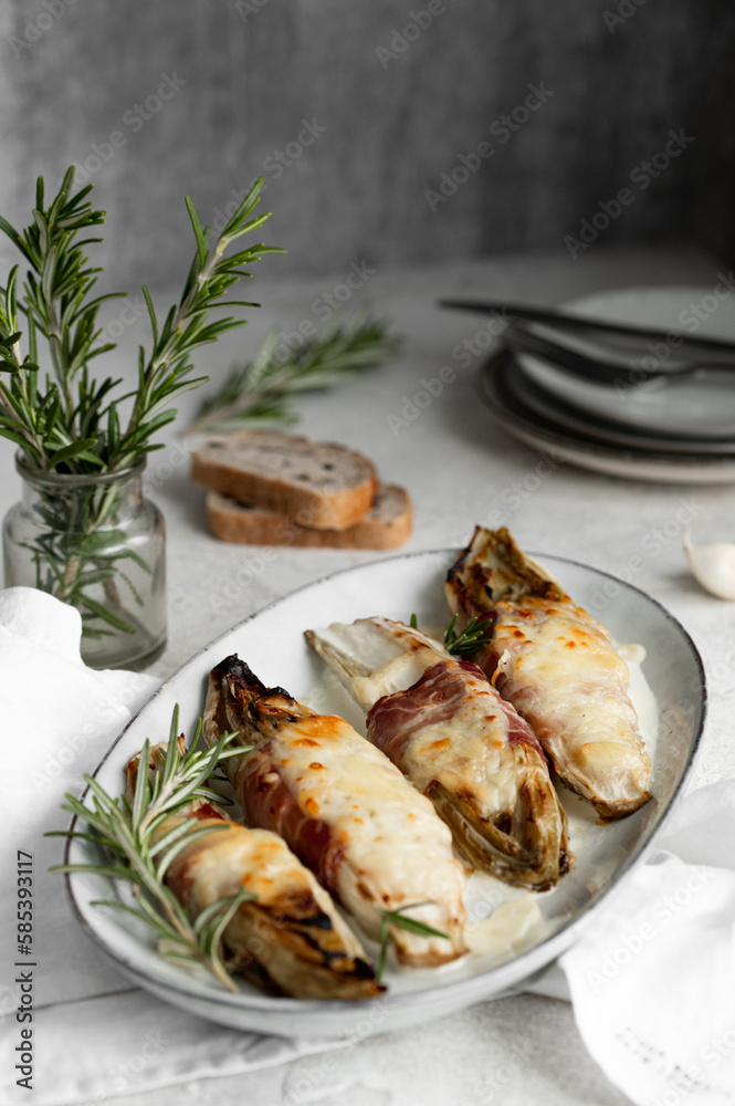 Braised chicory with ham, endives on a light stone background. Traditional Belgian cuisine. Braised chicory with ham, endives on a light stone background. Traditional Belgian cuisine.