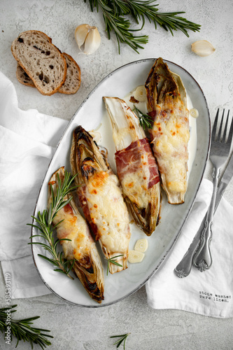 Foto Braised chicory with ham, endives on a light stone background