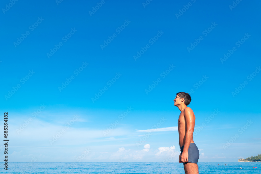 The figure of a young tanned guy on the beach against the background of the blue sea and sky.