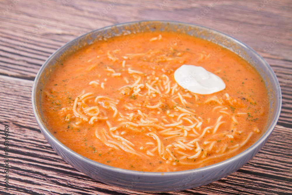 Tomato soup with noodles and a spoonful of cream on a wooden background Tomato soup with noodles and a spoonful of cream on a wooden background