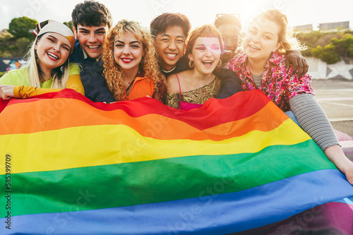 Young diverse people having fun holding LGBT rainbow flag outdoor - Focus on center girl face