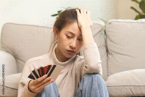 Financial owe asian young woman, girl sitting suffer, stressed and confused, sitting and holding many credit card, no money to pay expense, mortgage or loan. Debt, bankruptcy or bankruptcy concept.