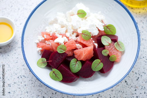 Salad with beetroot, feta cheese and grapefruit served in a white plate, horizontal shot on a light-grey granite background, middle close-up