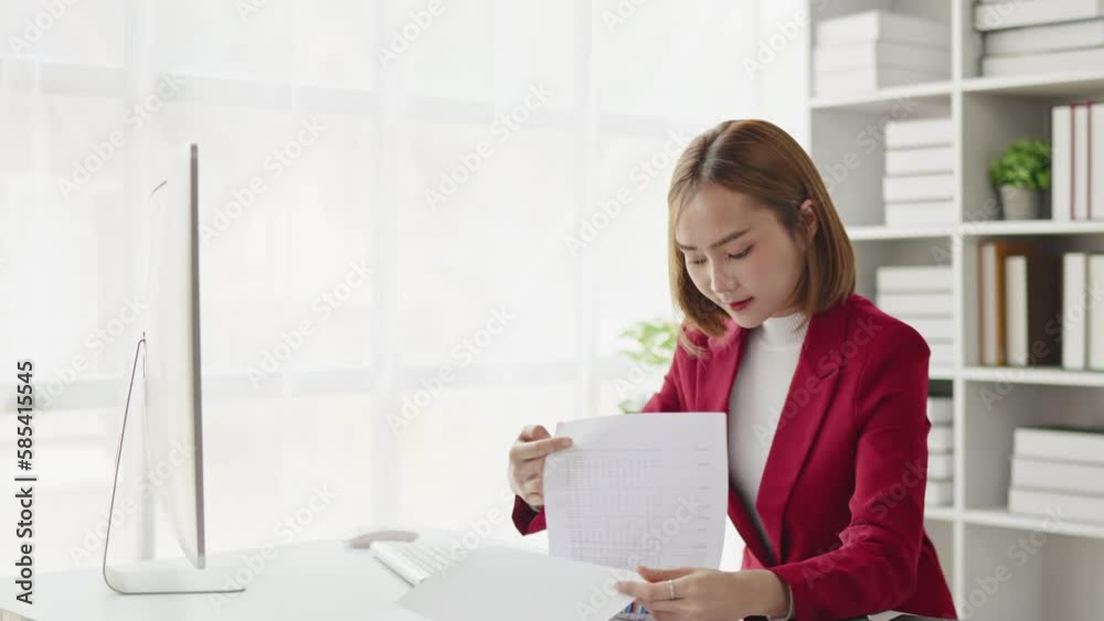 Businesswoman in red suit working on laptop and paperwork that show cost planning accounting numbers tables on office space. Businesswoman in red suit working on laptop and paperwork that show cost planning accounting numbers tables on office space.