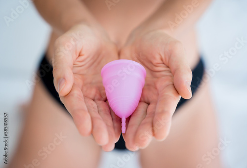 Young beautiful woman at home holding a menstrual cup in her hands