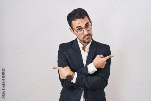 Handsome business hispanic man standing over white background pointing to both sides with fingers, different direction disagree