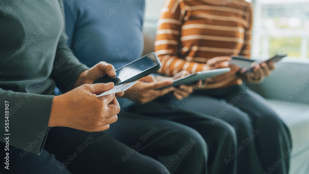 My device of three people as mother, daughter and friends watching social media news, using laptop computer, tablet pc and mobile cell phone on sofa.