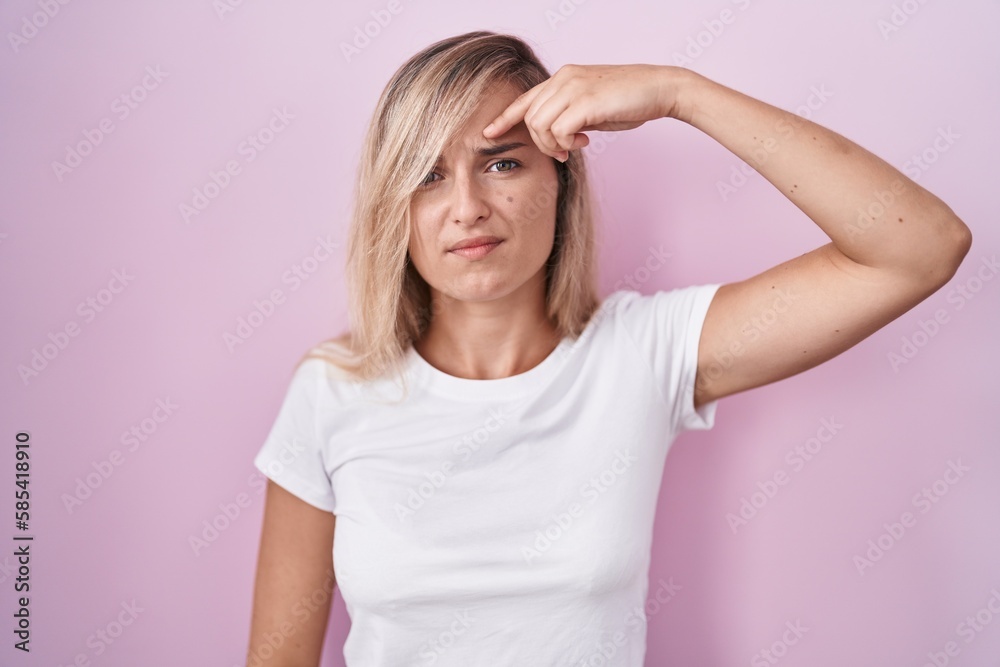 Young blonde woman standing over pink background pointing unhappy to pimple on forehead, ugly infection of blackhead. acne and skin problem Young blonde woman standing over pink background pointing unhappy to pimple on forehead, ugly infection of blackhead. acne and skin problem