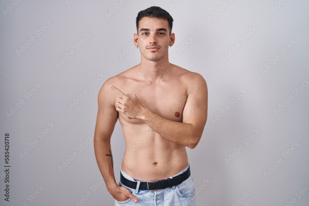 Handsome hispanic man standing shirtless pointing with hand finger to the side showing advertisement, serious and calm face